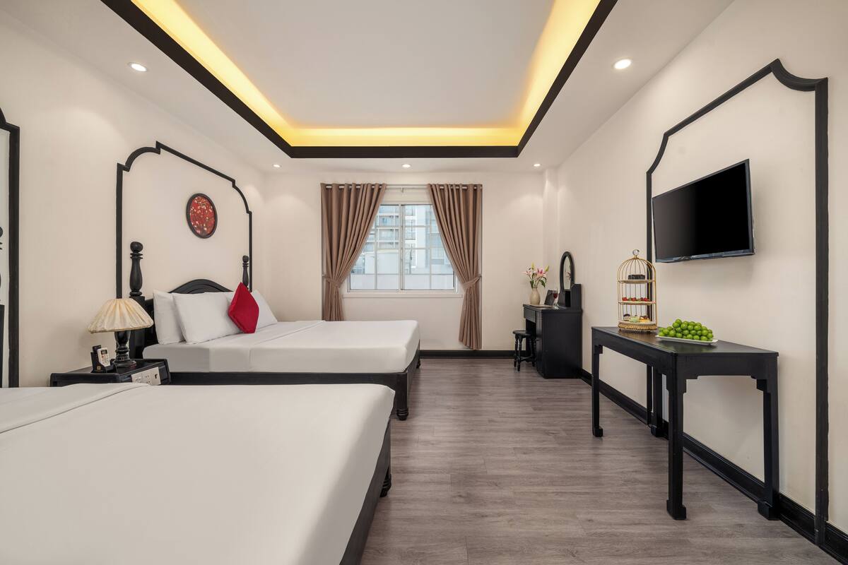 Habitación de hotel con dos camas, un escritorio, un televisor y una ventana con cortinas.