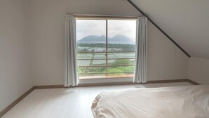 A bedroom with a large window, a bed, and a view of a landscape with mountains and a body of water. - Lake Toya and Nakajima (Toyako)