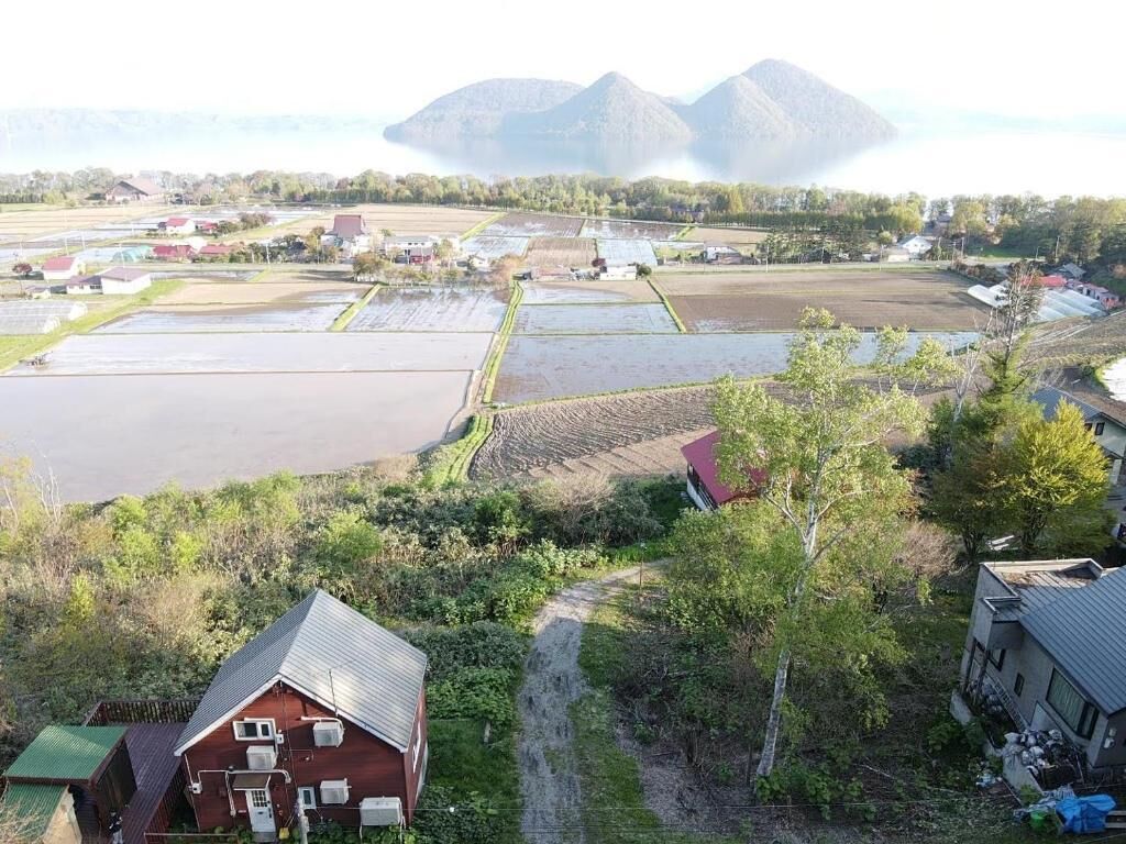 A rural landscape with fields, a small house, and distant mountains.