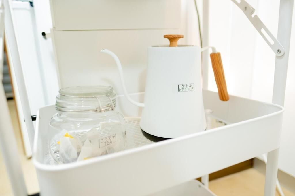 A white kettle and a glass jar with tea bags on a white tray.