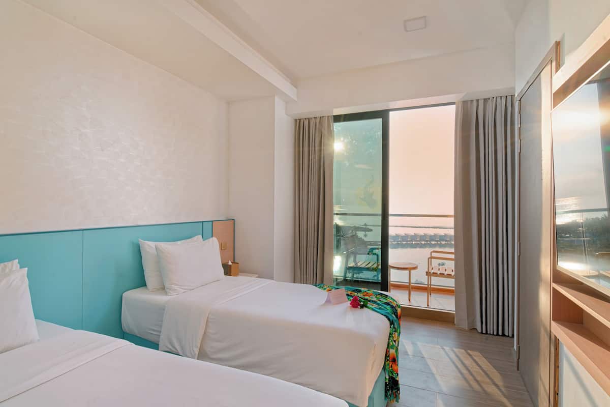 A hotel room with two beds, a balcony with a view, and a large window with curtains.