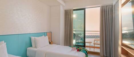 A hotel room with two beds, a balcony with a view, and a large window with curtains.