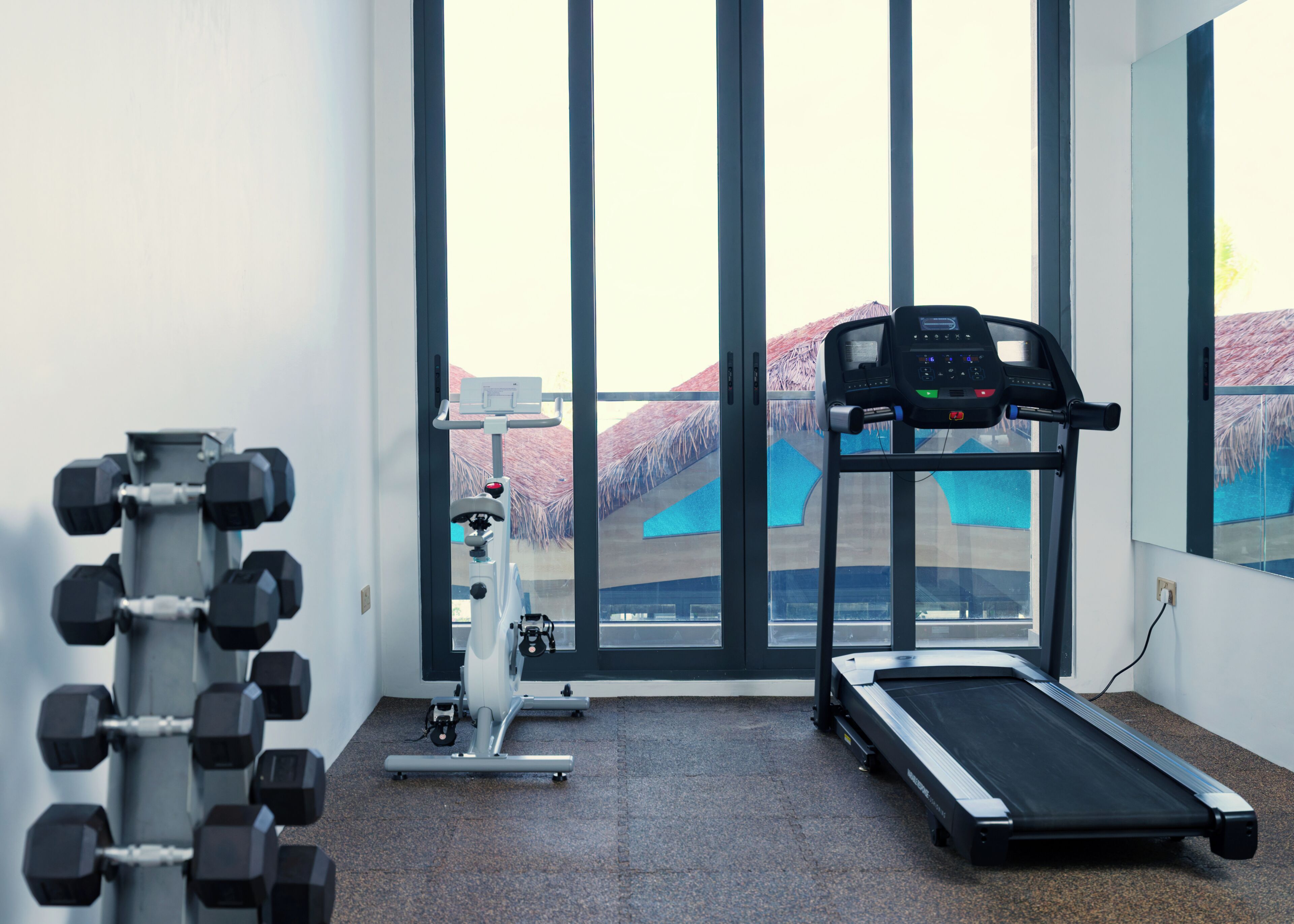 Een sportschool met fitnessapparatuur, grote ramen en een loopband.