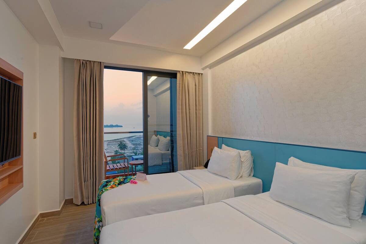 A hotel room with two beds, a balcony with a view, and a large window with curtains.