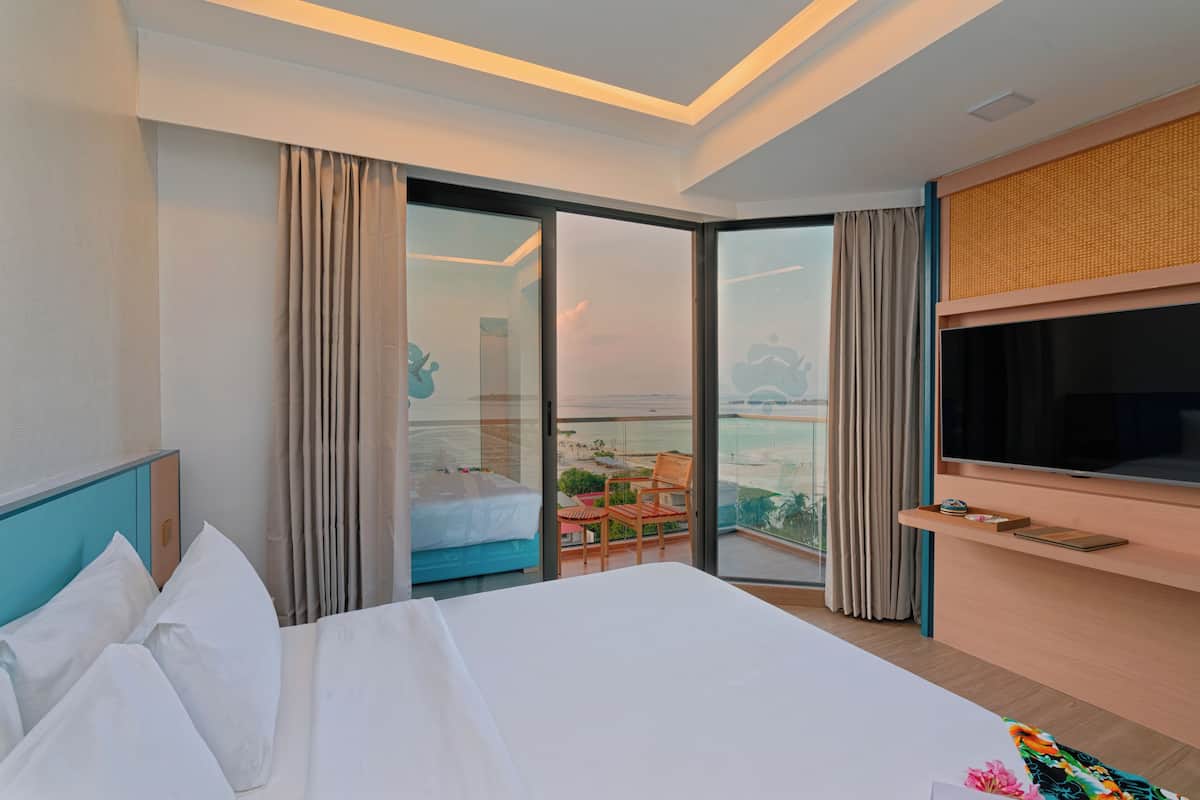 A hotel room with a bed, a TV, a balcony with a view, and a sliding door to a balcony area.