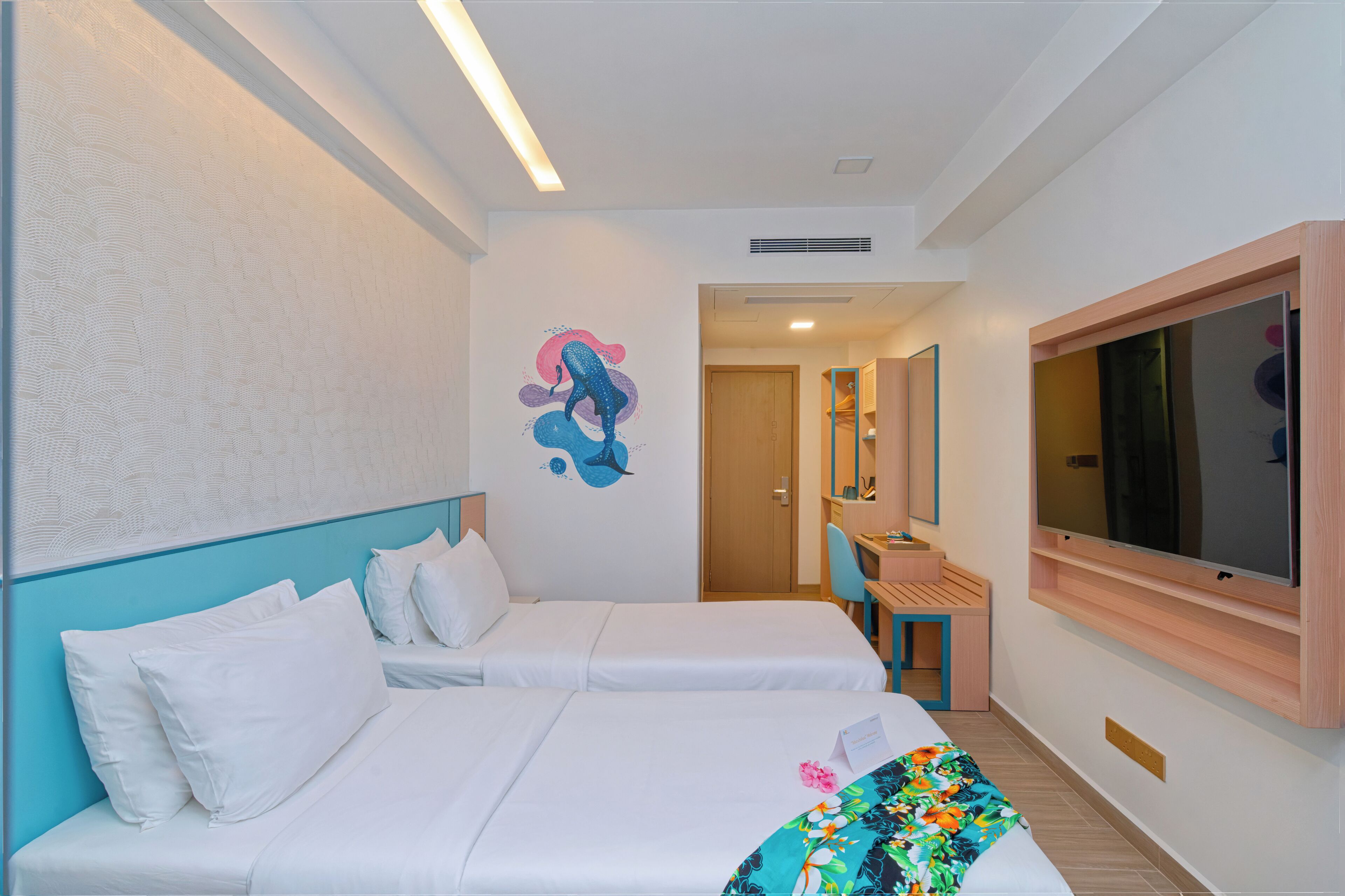 A hotel room with two beds, a desk, a chair, a TV, and a wall mural.
