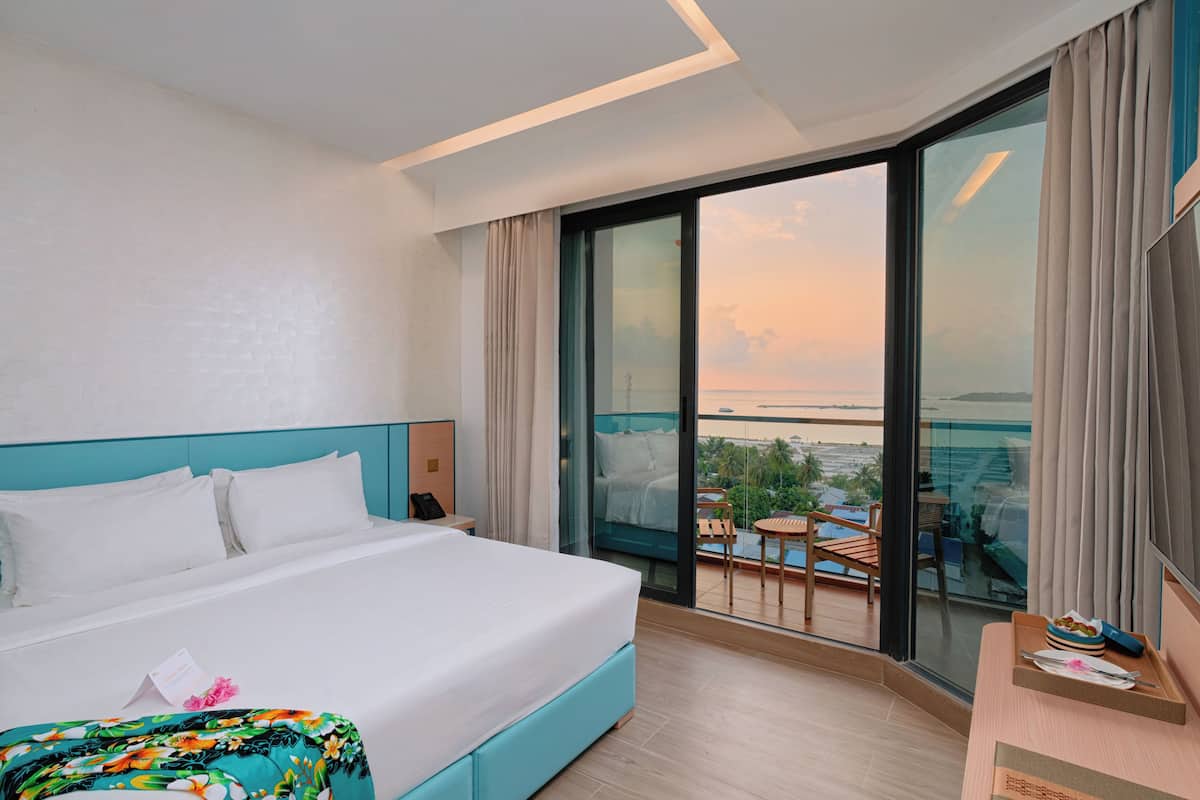 A hotel room with a large bed, a balcony with a view of the sea, and a small table with a tray.