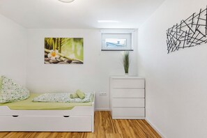A bedroom with a bed, a window, a wall-mounted picture, and a white cabinet.