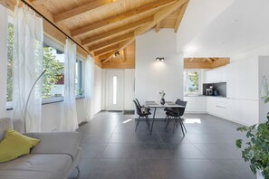 A modern kitchen with white cabinets, a dining area with a table and chairs, and a living room with a sofa and a plant. - Apartment 'Casa Verde - Moos' with Private Terrace, Shared Garden and Wi-Fi (Moos)
