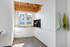 A modern kitchen with white cabinets, a wooden ceiling, a window, and a sink.