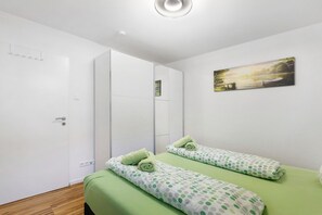 Une chambre avec deux lits, une armoire blanche, un tableau et un plancher en bois.