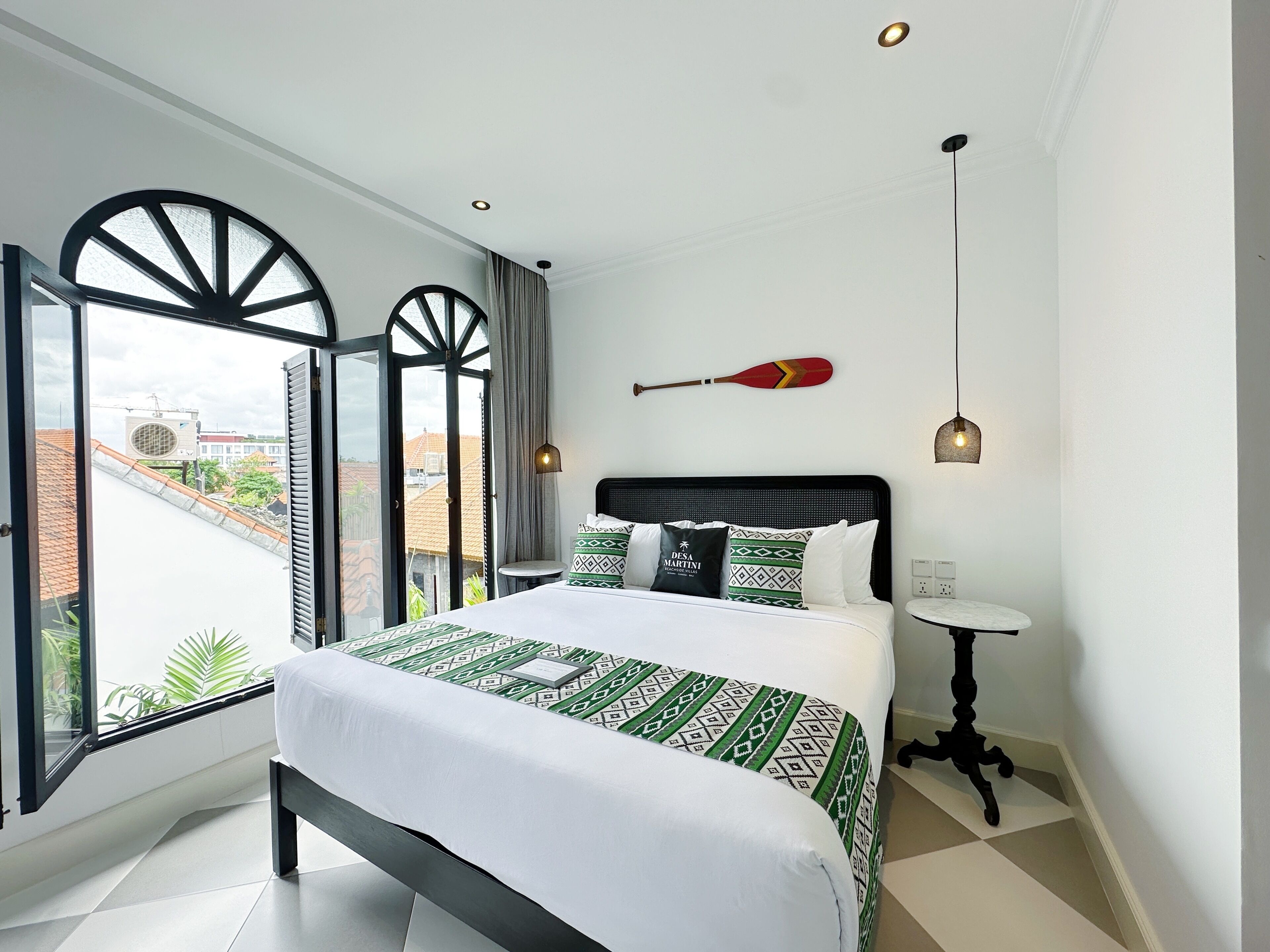 Une chambre d’hôtel avec un lit, une petite table et une vue sur le paysage urbain, visible à travers de grandes fenêtres.