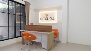 Un espace de bureau moderne comprenant un bureau, deux chaises orange, une grande fenêtre avec vue et un panneau indiquant « NEXURA ».