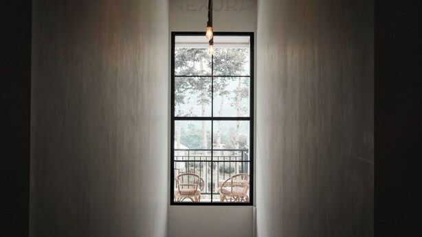 Un couloir étroit, avec une grande fenêtre au fond, donnant sur du mobilier de jardin et des arbres.