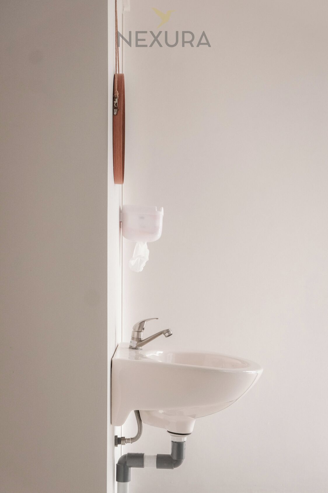 A white wall-mounted sink with a modern faucet, a soap dispenser, and a towel hanging on a towel rack.