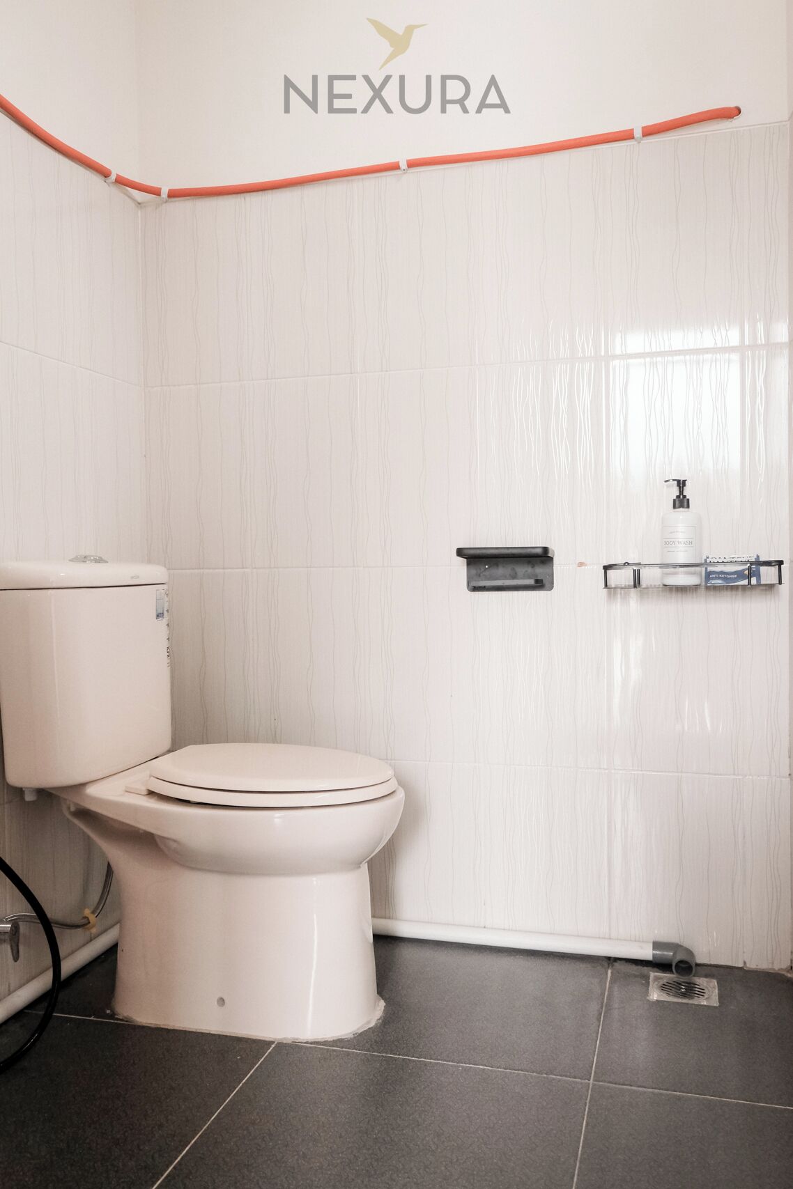 Een badkamer met een wit toilet, een zeepdispenser en een klein plankje.