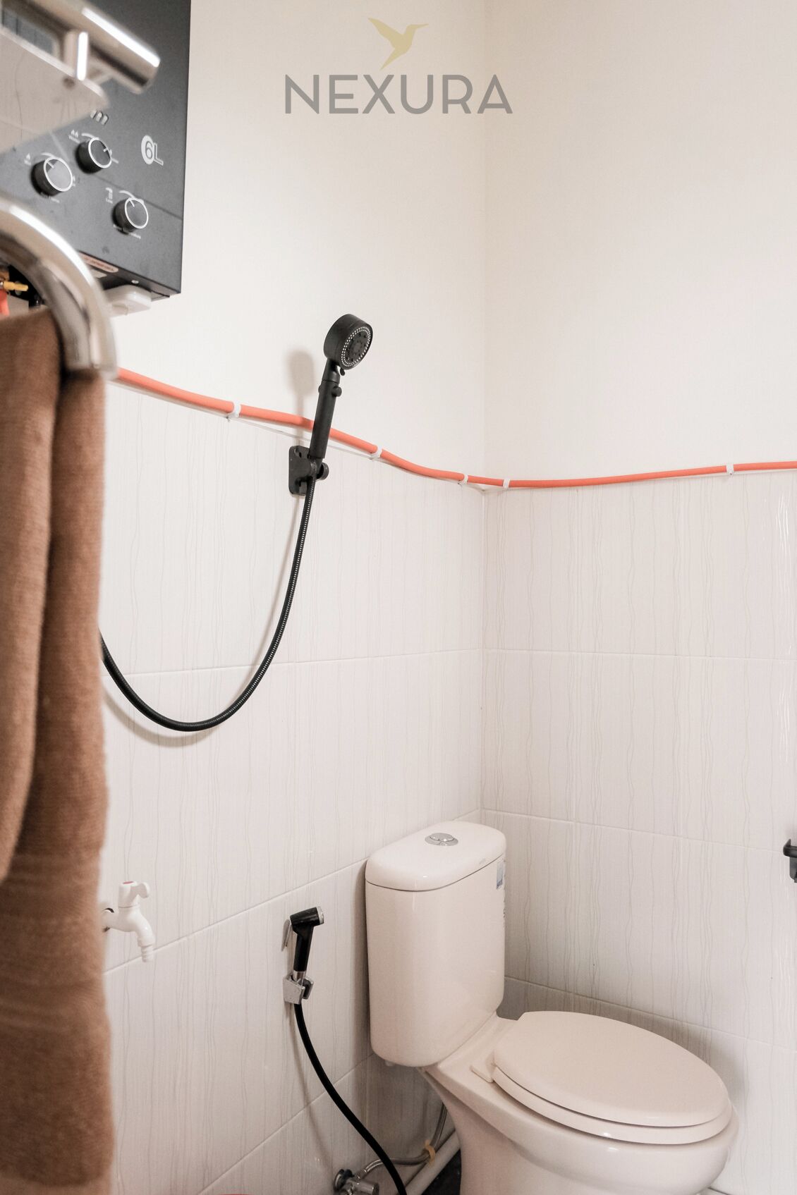 A bathroom with a white toilet, a shower head, and a towel hanging on a rack.