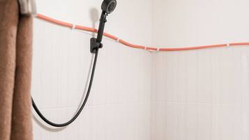 A bathroom with a white toilet, a shower head, and a towel hanging on a rack.