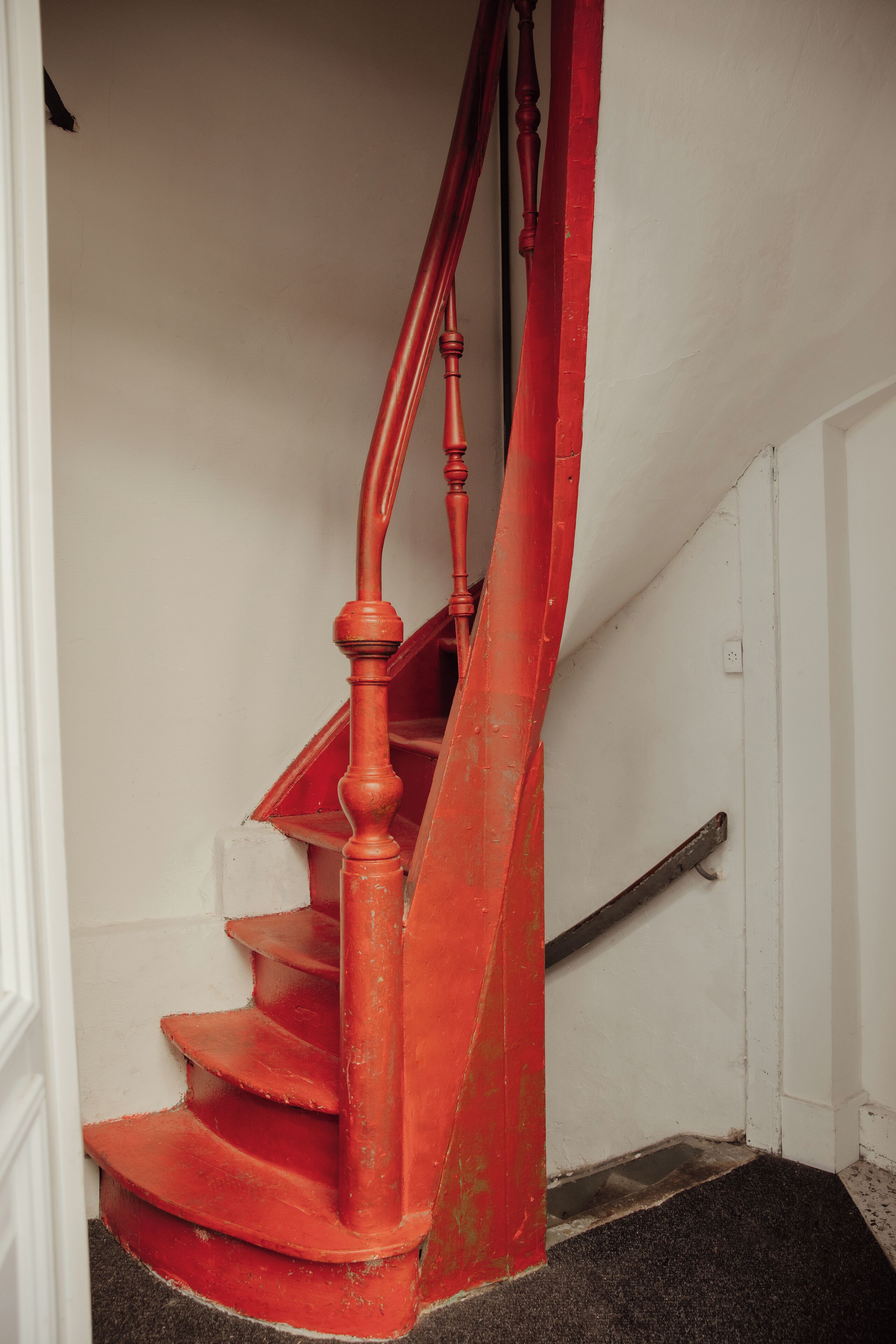 Una escalera espiral roja con barandilla de madera y un rellano cubierto de alfombra negra.