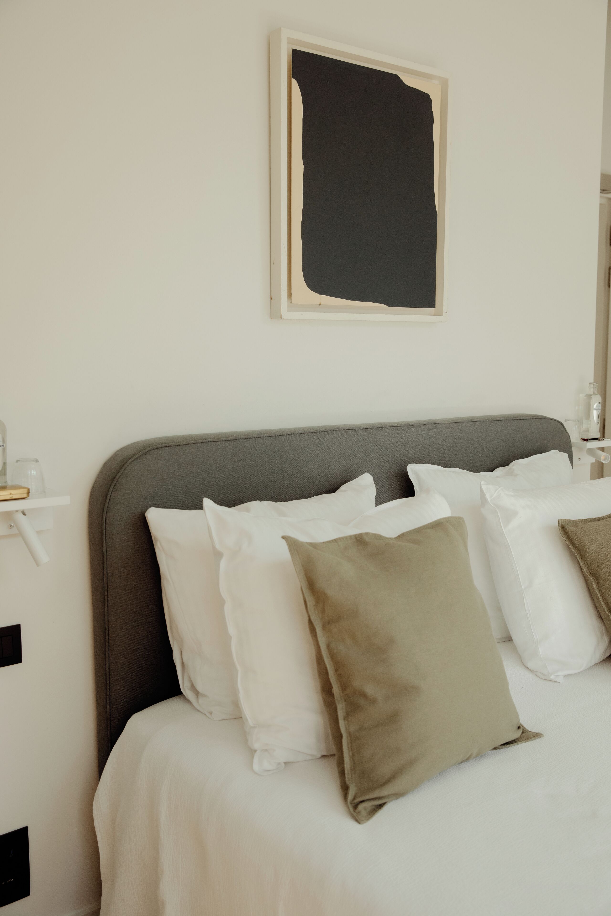 A neatly made bed with white and beige pillows, a gray headboard, and a simple wall-mounted artwork.
