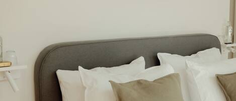 A neatly made bed with white and beige pillows, a gray headboard, and a simple wall-mounted artwork.
