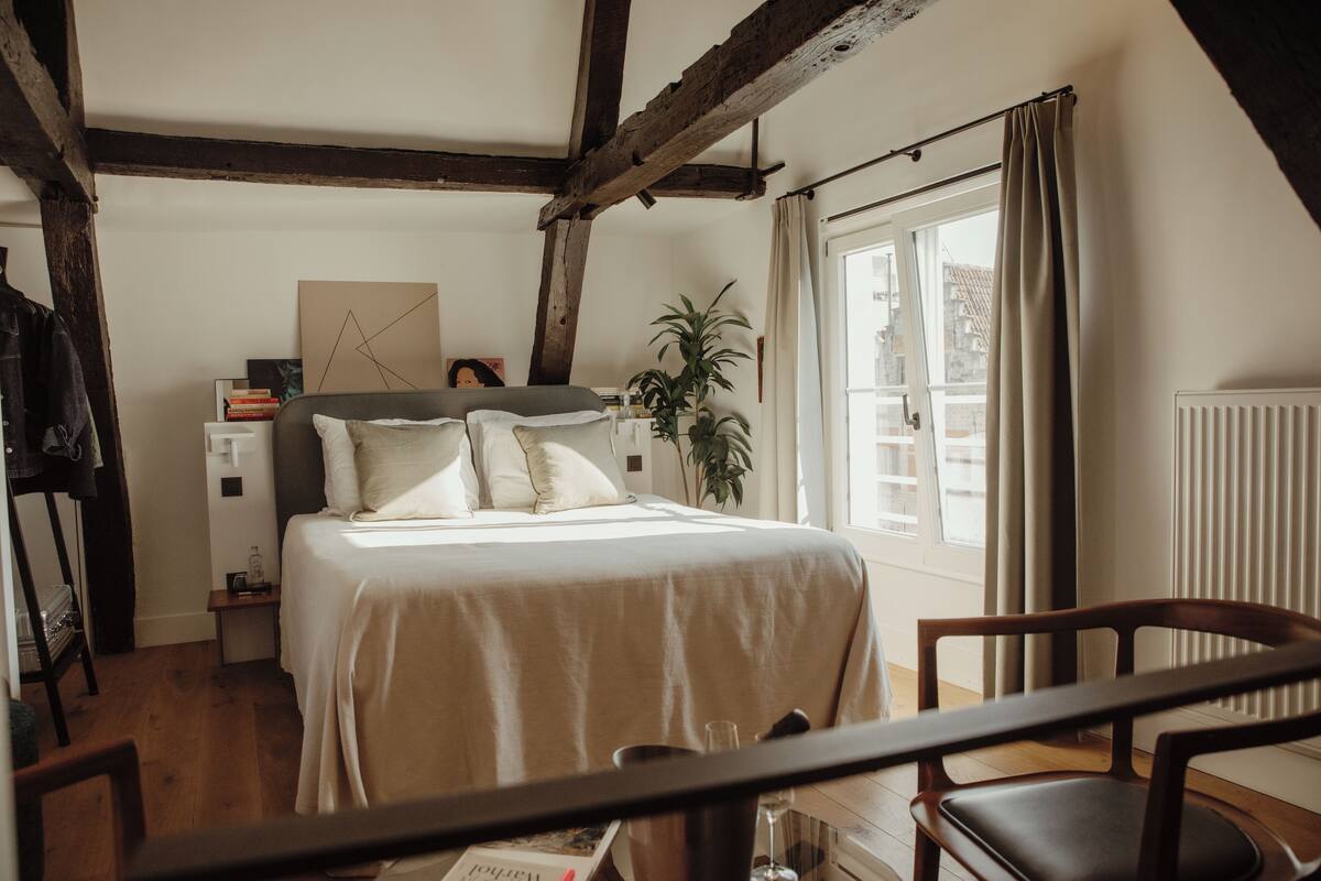 Ein Schlafzimmer mit Bett, Nachttisch, Stuhl, Fenster und einer Pflanze.
