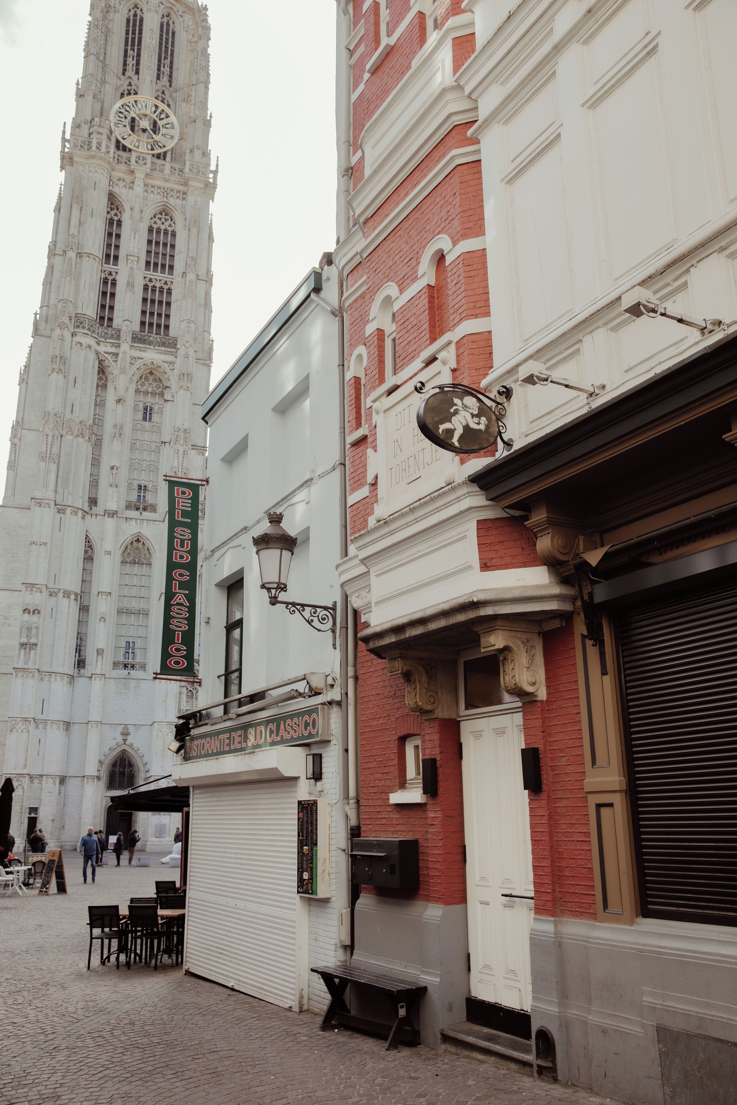 A historic building with a clock tower, a restaurant sign, and a closed shuttered entrance.