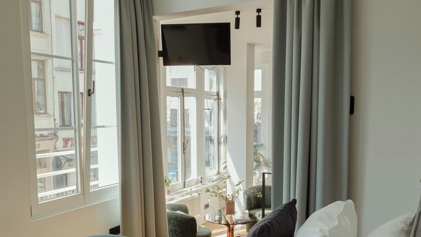 A hotel room with a bed, a TV, a window with curtains, and a breakfast tray on the windowsill. - A Place - Oude Koornmarkt 1 (Antwerp)