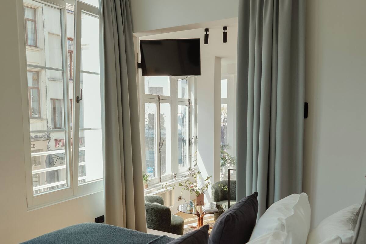Ein Hotelzimmer mit Bett, Fernseher, Fenster mit Vorhängen und Tablett mit Frühstück auf der Fensterbank.