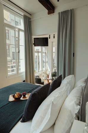 Habitación de hotel con cama, televisión, ventana con cortinas y bandeja de desayuno en el alféizar.