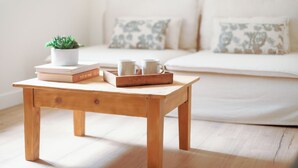 Een houten tafel met boeken, een kleine plant en twee mokken voor een bed met gestreepte kussens.