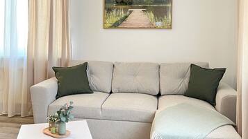 Una sala de estar con un sofá seccional color beige, una mesa de centro blanca y un cuadro de un lago y un muelle.