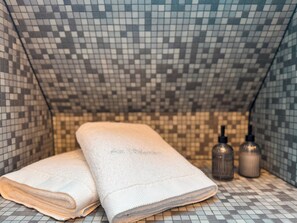 Un baño con piso y paredes de azulejos, una toalla doblada y dos botellas.