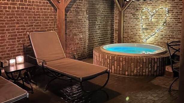 A covered outdoor area with a brick wall, a hot tub, and a lounge chair.