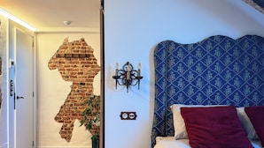 A bedroom with a sloped ceiling, a brick wall mural, a bed with patterned headboard, a nightstand, and a colorful rug.