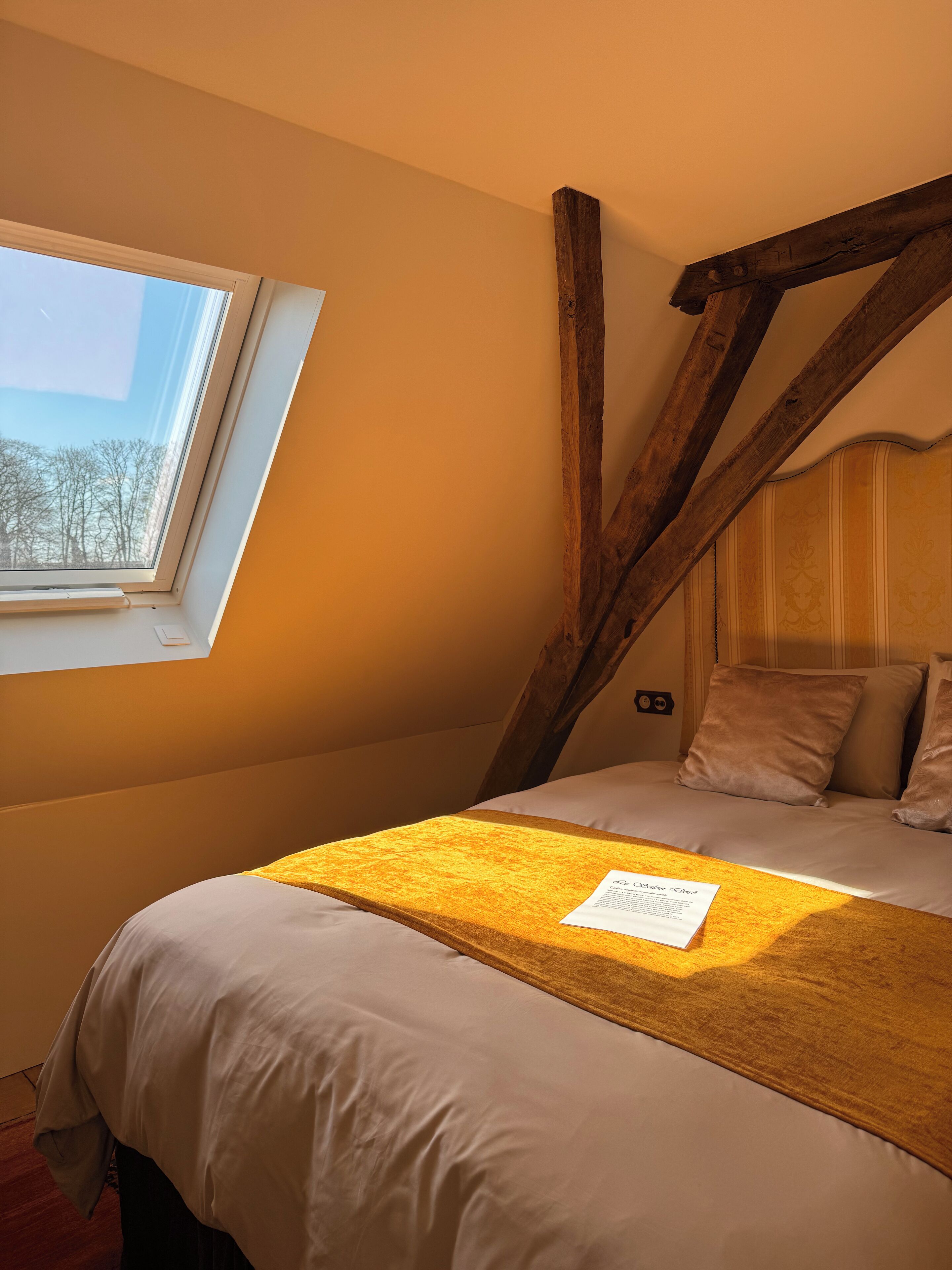 A bedroom with a sloped ceiling, a window, and a bed with a yellow throw blanket.