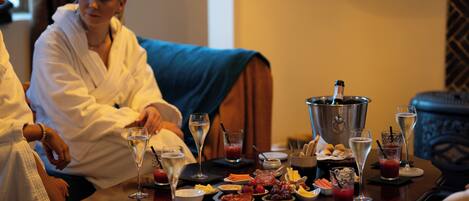 A dining table with various food items and drinks, a bottle of champagne, and a bucket.
