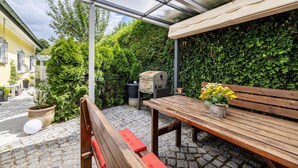 A covered patio with a wooden table and bench, a grill, and a potted plant. - Apartment “Haus Fabio” with Private Terrace and Wi-Fi (Engstingen)