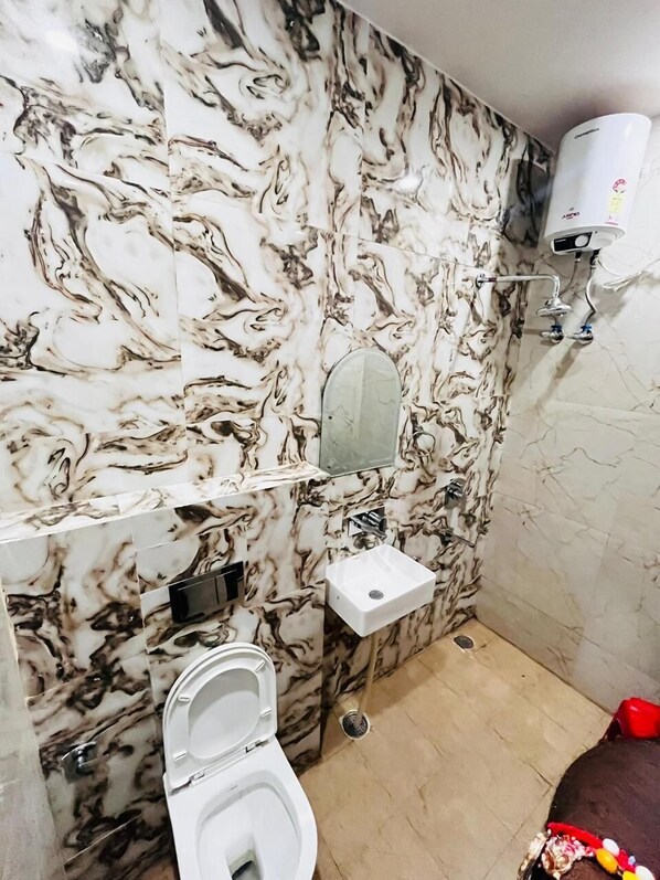 A bathroom with a marble wall, a white sink, a toilet, and a shower.