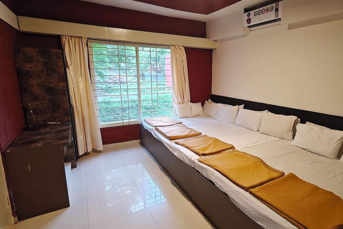 A hotel room with a large bed, a window with curtains, a small table, and a thermostat on the wall.