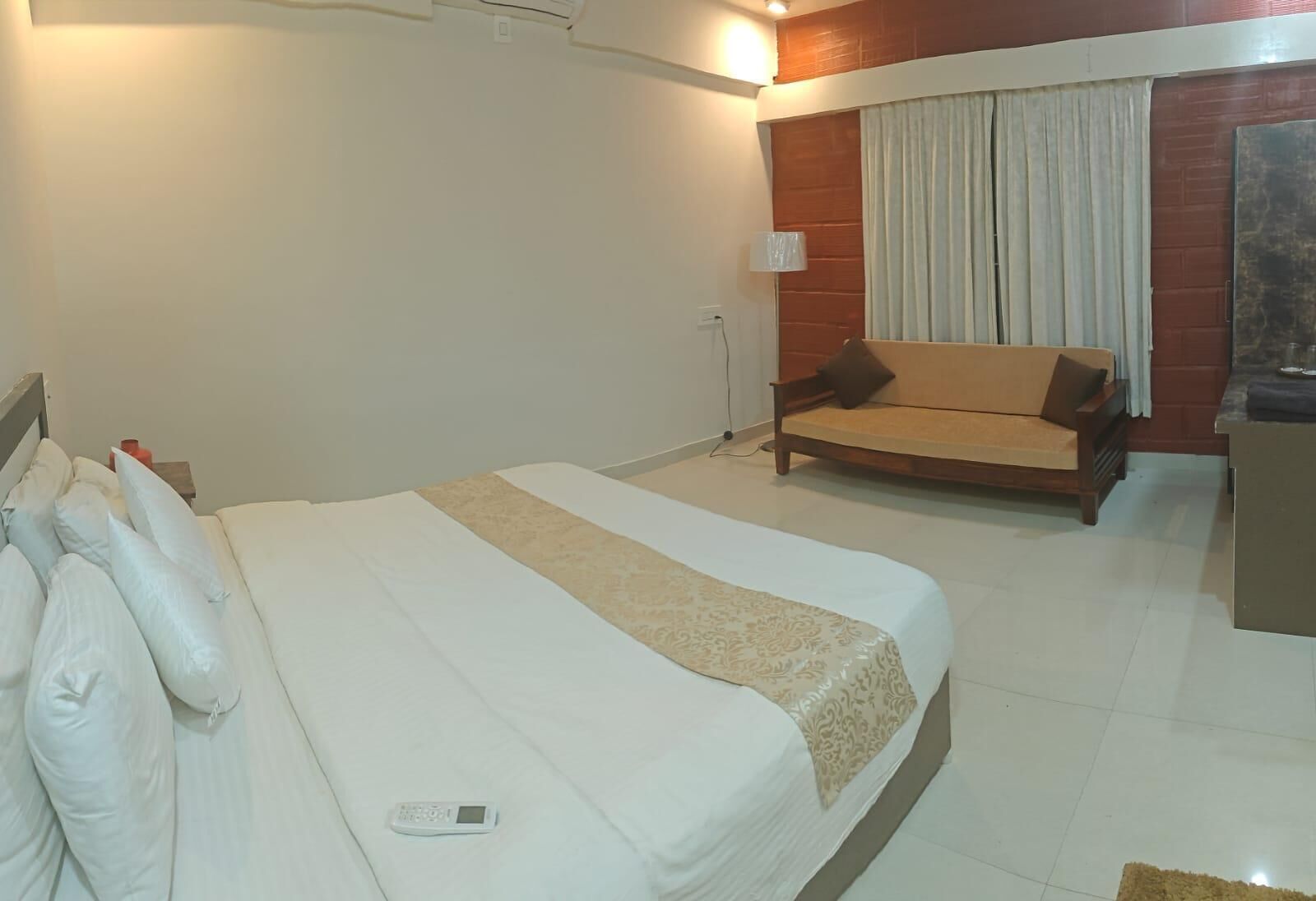 A hotel room with a large bed, a sofa, a lamp, and a window with curtains.