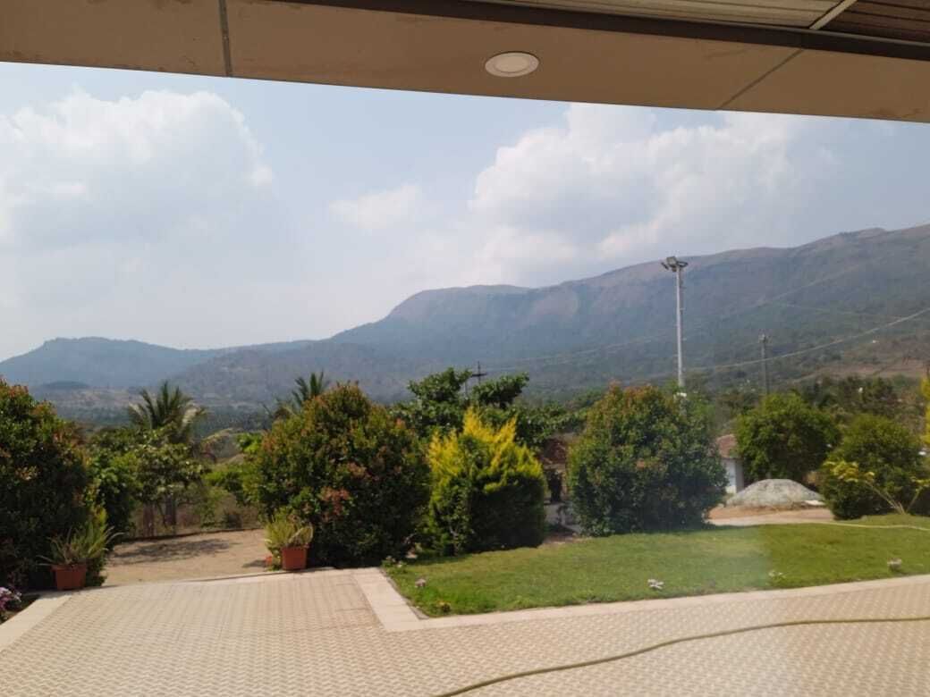 A view from a covered outdoor area with a paved floor, surrounded by greenery and a distant mountain range.