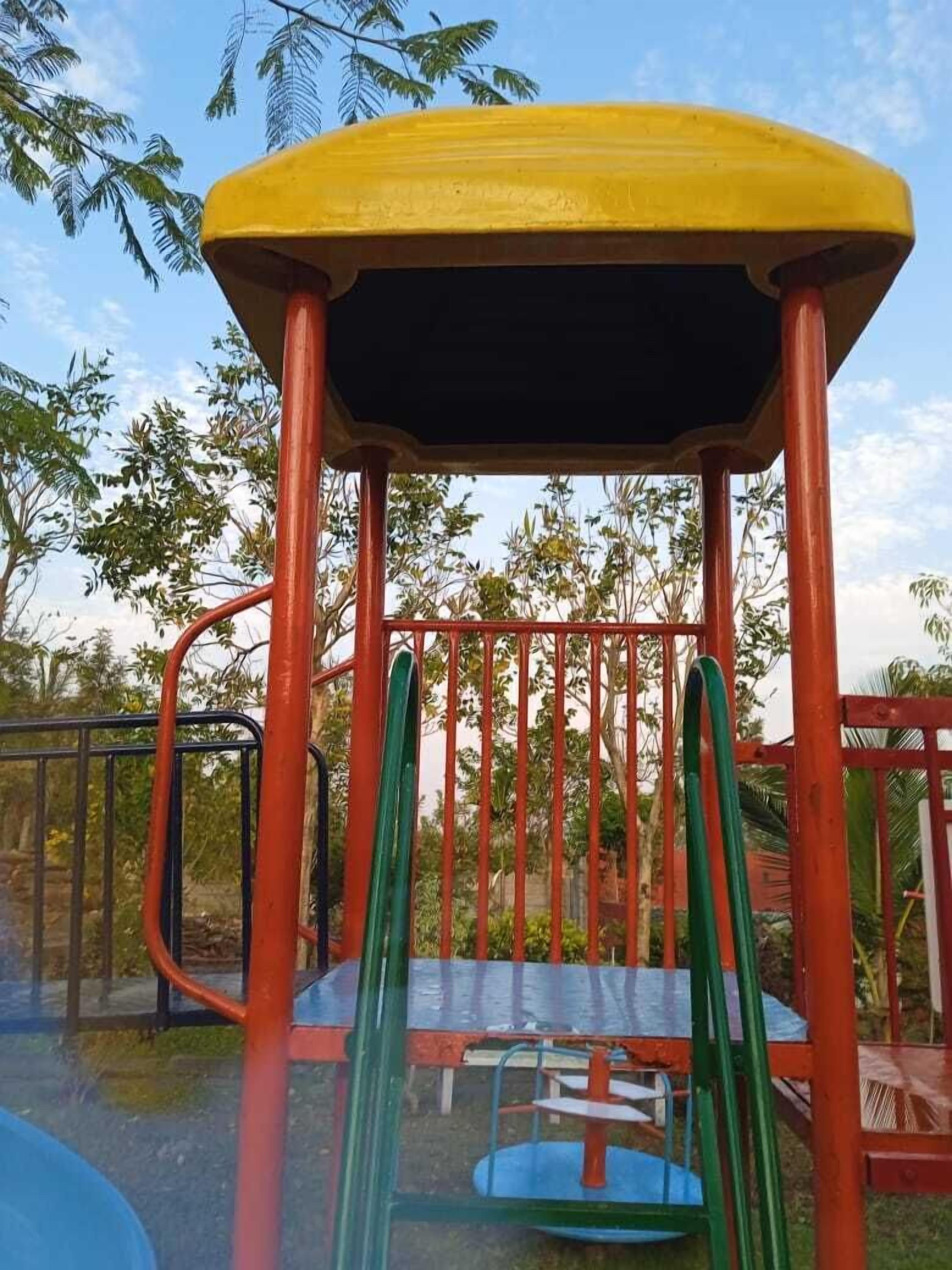 A playground structure with a yellow roof, red and green poles, and a blue and red play table.