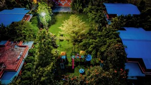 Luftaufnahme eines Parks mit Spielgeräten, umgeben von Bäumen und Gebäuden mit blauen Dächern.