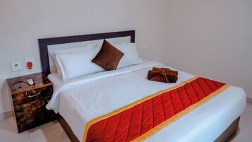Una cama bien hecha con colcha roja y blanca, una mesita de noche de madera con un control remoto y un ventilador de pared.