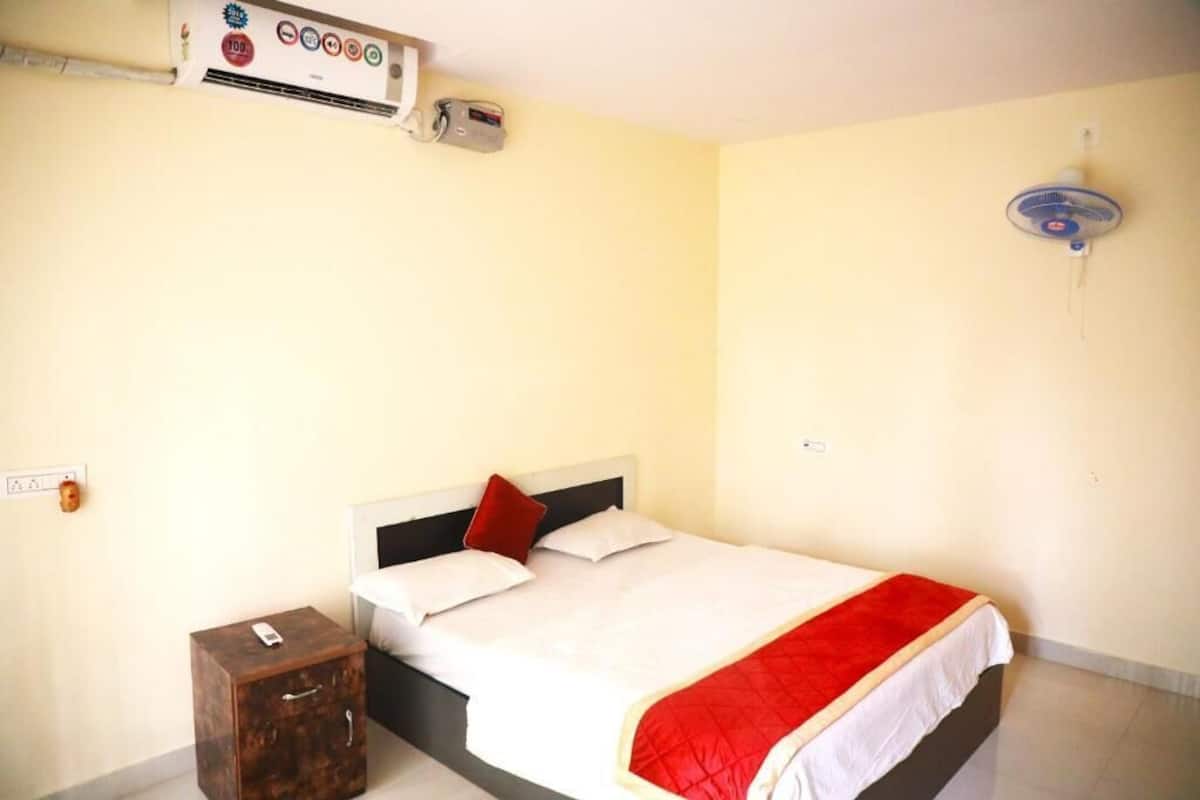 A hotel room with a bed, a bedside table, a wall-mounted air conditioner, and a ceiling fan.