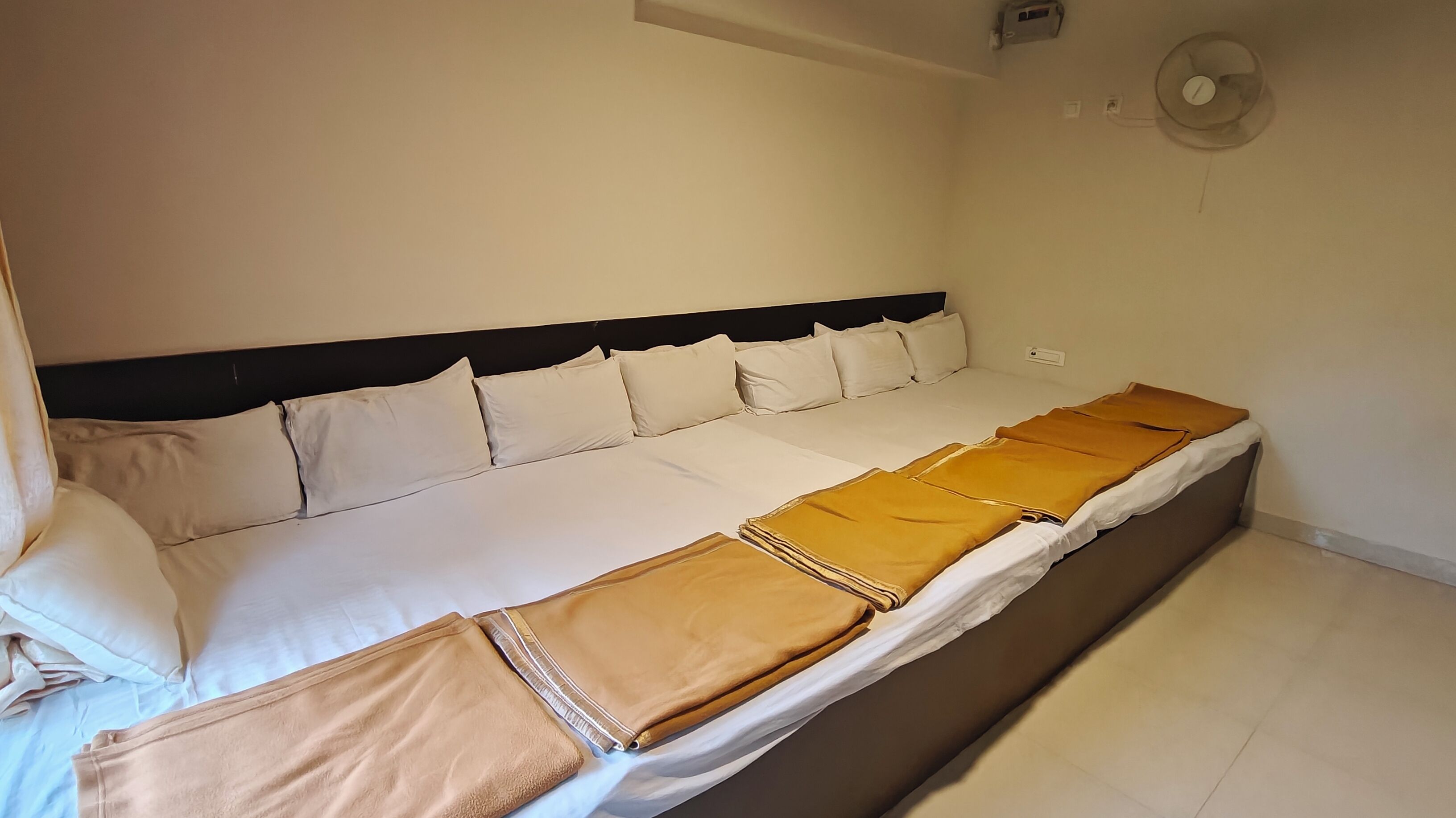 A neatly made bed with white linens and a brown blanket, a black headboard, and a wall-mounted fan.