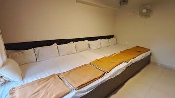 Cama bem arrumada com lençóis brancos e manta marrom, cabeceira preta e ventilador fixado na parede.