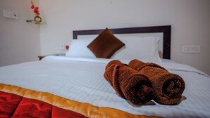 Ein ordentlich bezogenes Bett mit einem braunen Handtuch, weißer Bettwäsche und einem rot-gelben Akzent am Fußende.