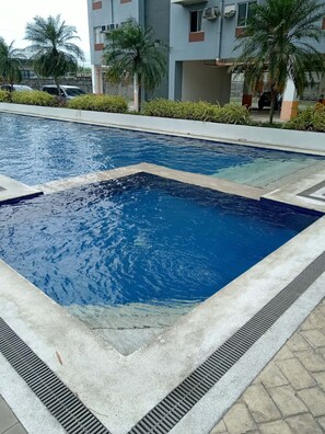 Une piscine dont le bord est revêtu de carreaux, entourée d’une allée dallée.